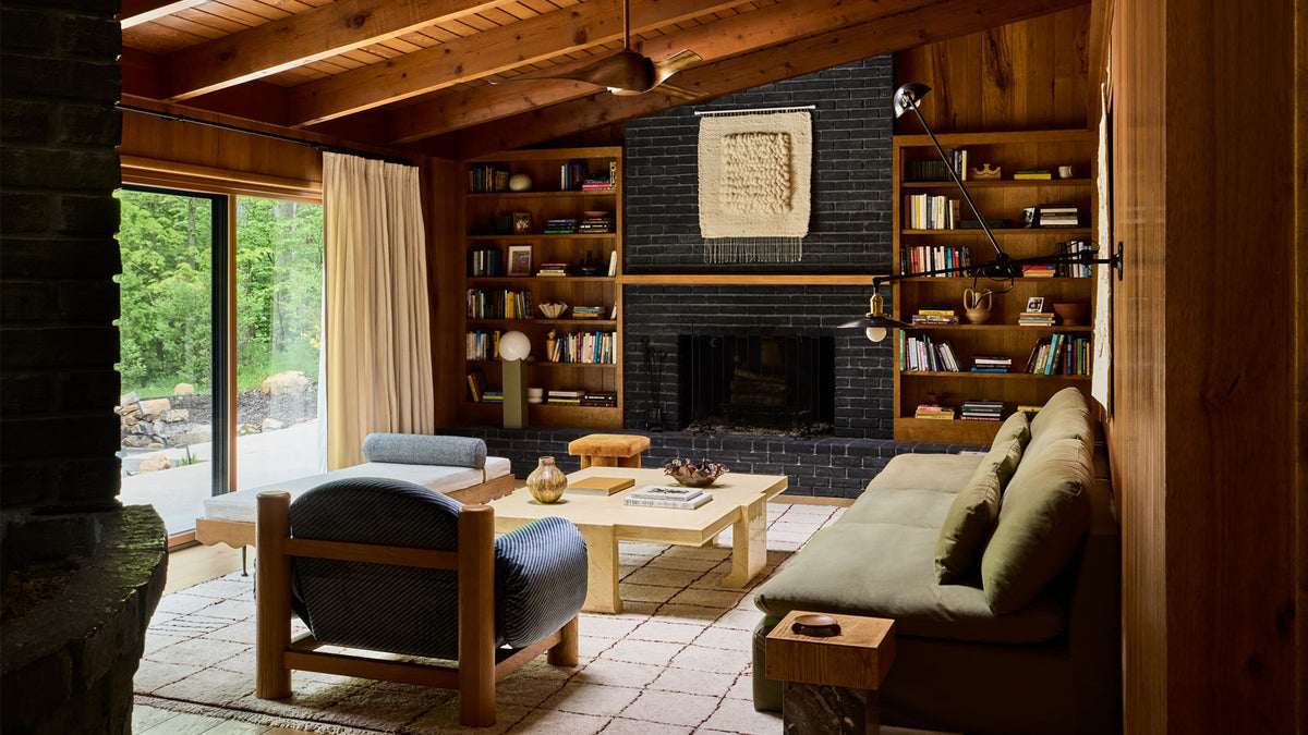 A cozy, living room with a wood-paneled ceiling, a dark brick fireplace, built-in bookshelves, a light wood coffee table, a blue upholstered armchair, and a green sofa.