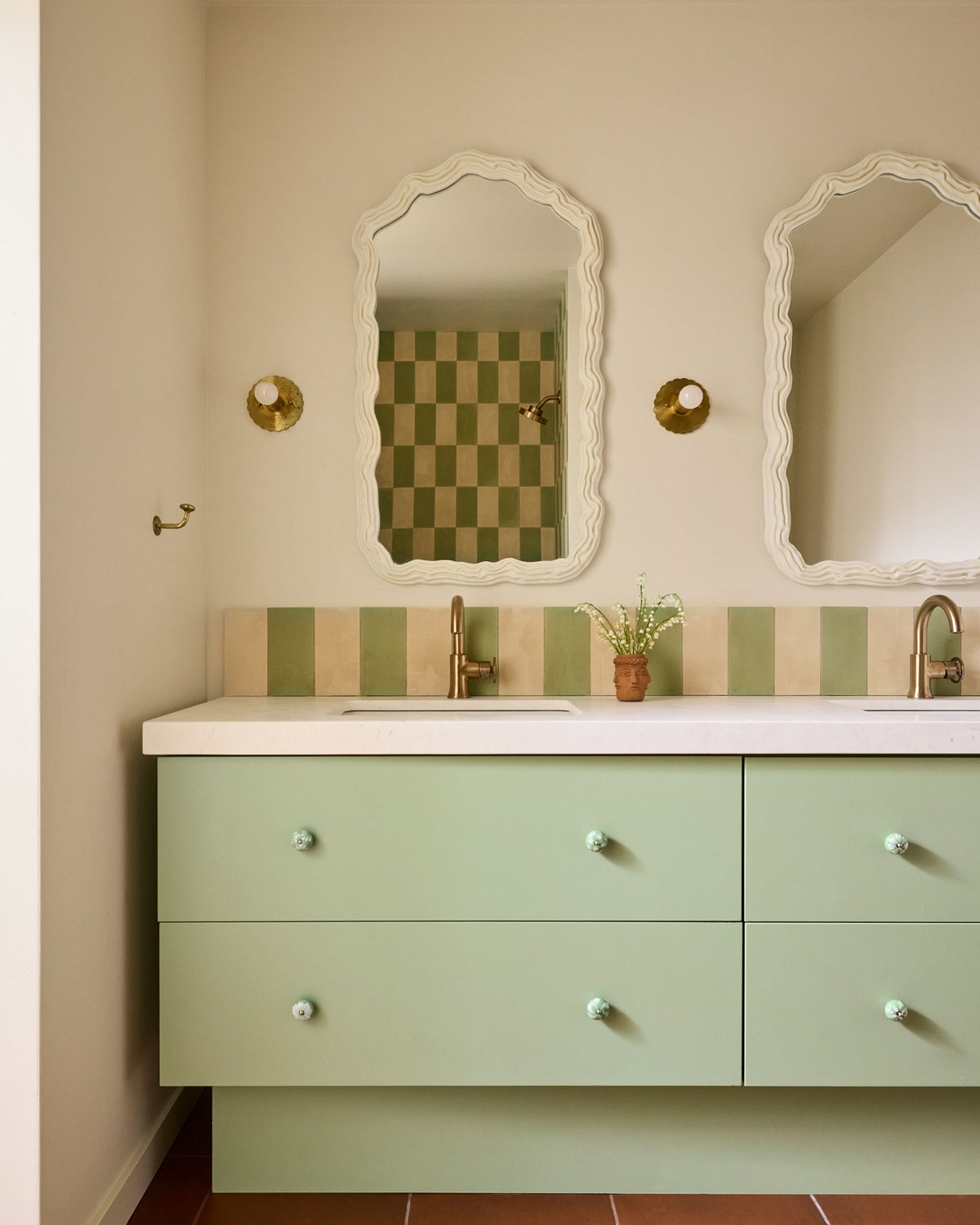 A bathroom vanity with pale green drawers, a white countertop, a striped tile backsplash, and two ornate white-framed mirrors on a beige wall.