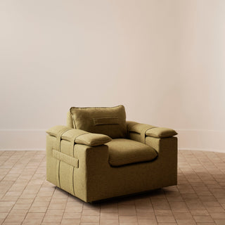 An olive green upholstered armchair with a matching back cushion, set against a minimalist beige wall and tiled floor.