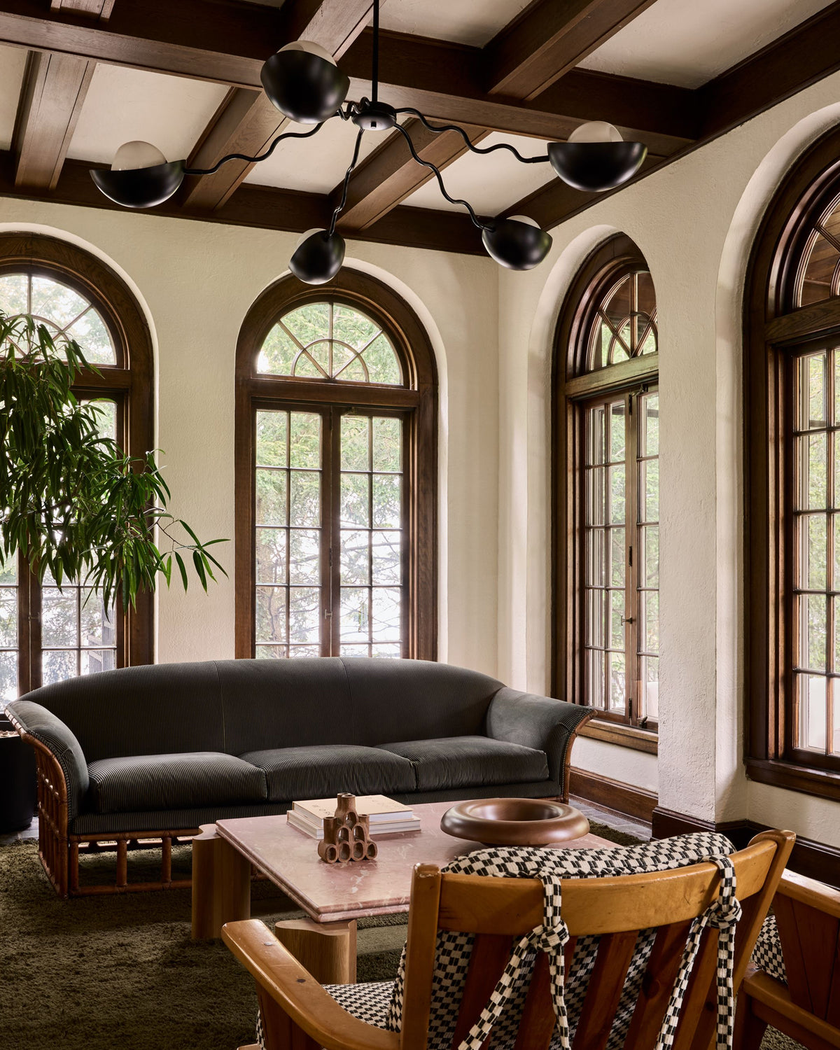 A striped velvet sofa in an elegant living room with arched windows, dark wood ceiling beams, and a black multi-light chandelier.
