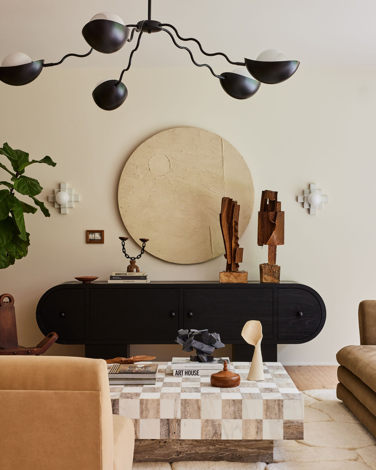 A styled living room interior featuring a black mid-century modern multi-arm chandelier, a black console table, a checkerboard coffee table, and warm neutral decor against a beige wall.